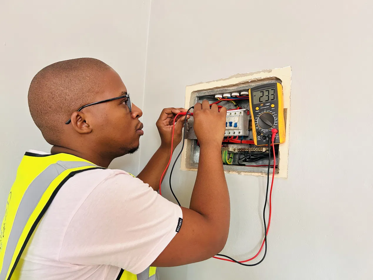 Gridsmith electrician in hi-vis vest testing a DB board with a multimeter